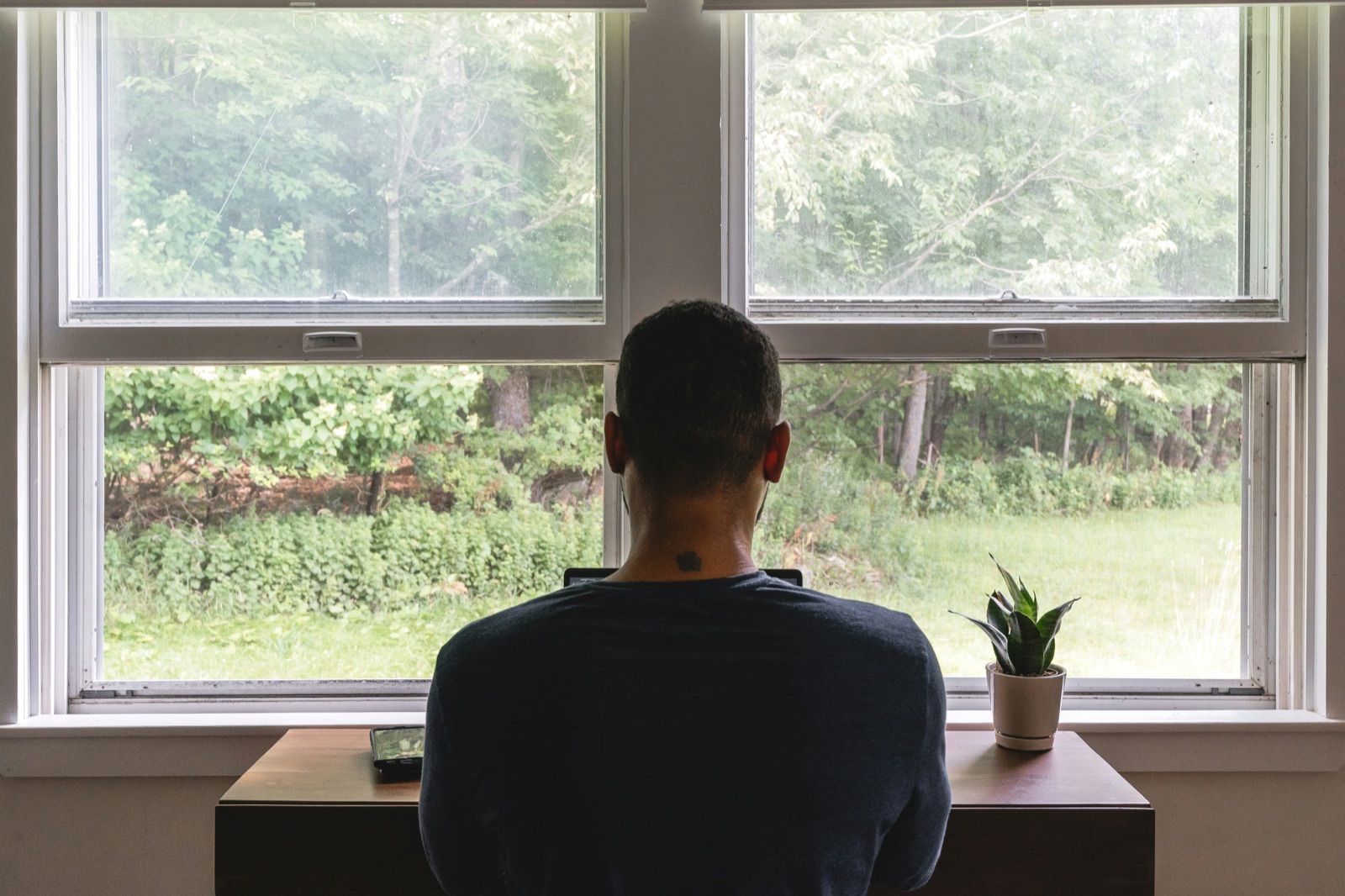 Man sitting alone looking out a window, representing the quiet threshold that brings men to therapy