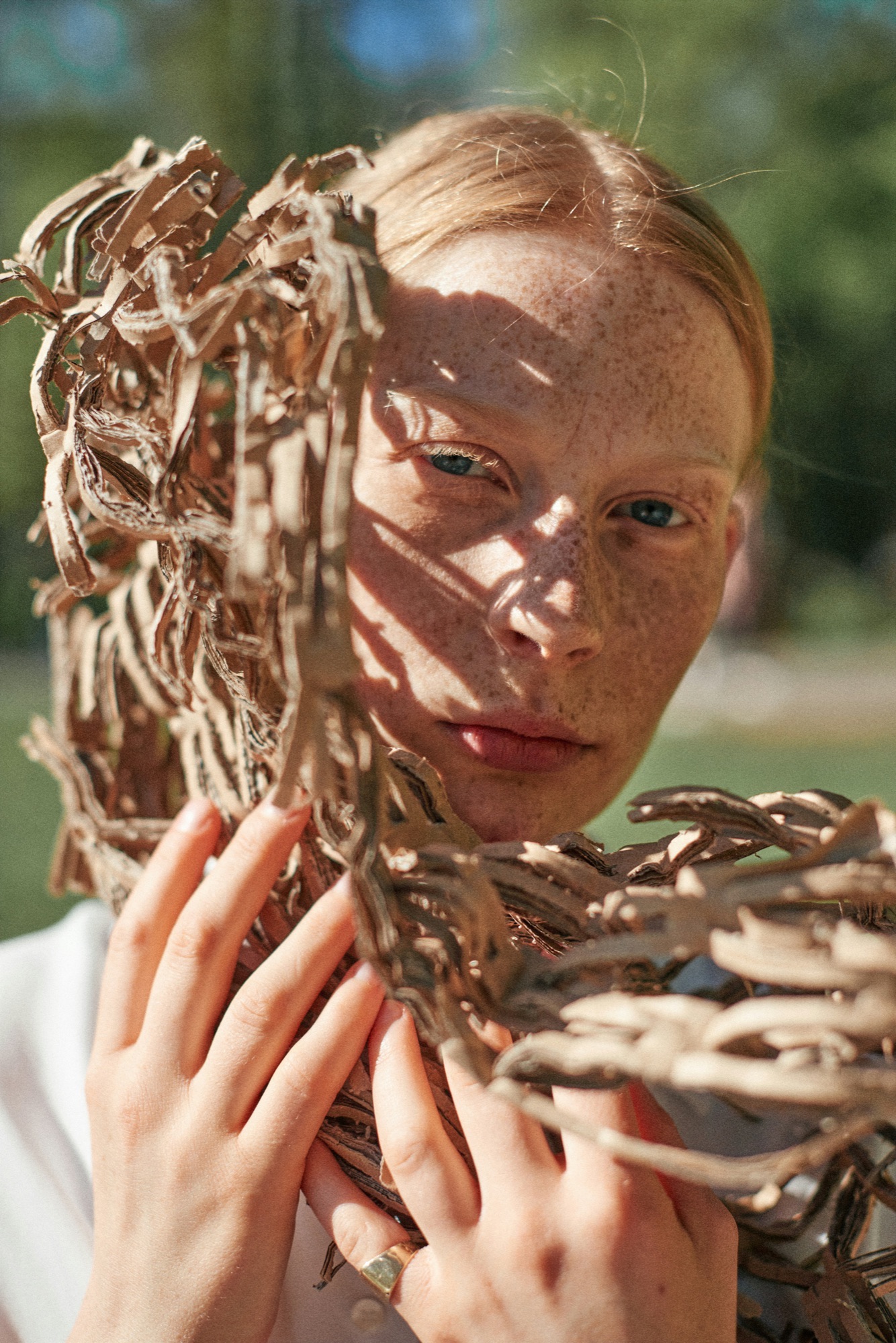 A person in dappled light holding woven dried branches close to their face